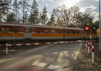 Widok z ziemi na przejazd kolejowo-drogowy i przejeżdżający po torach pociąg osobowy. 