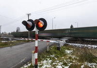 Widok z ziemi na przejazd kolejowo-drogowy i przejeżdżający po torach pociąg towarowy. 