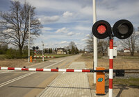 Widok z ziemi na przejazd kolejowo-drogowy, opuszczone szlabany i włączoną sygnalizację świetlną.