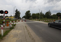 Widok z ziemi na przejazd kolejowo-drogowy. Widać samochody oczekujące na przejazd, zamknięte rogatki i sygnał świetlny.